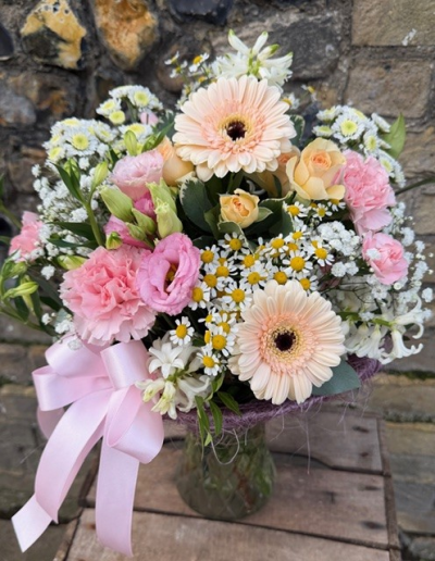 Blush Meadow Vase - A beautifully balanced vase arrangement in delicate pinks and peaches with airy white accents, presented in a textured glass vase and finished with a luxurious satin pink ribbon. A thoughtful gift that says it all.